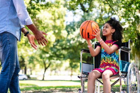 little girl wheelchair having fun with her father while playing basketball together park